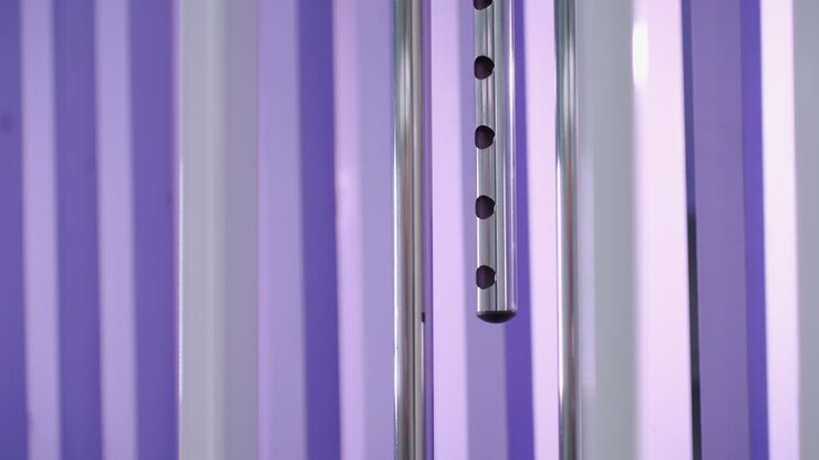 Primo piano di una pila di pesi che scende su un attrezzo da palestra con barre metalliche e uno sfondo viola vibrante, focus sul movimento e sull'allenamento di resistenza mentre il peso scende