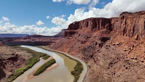 aerial view of highway in desert next to railroad tracks, tall red buttes in background, colorado river, potash road in moab utah
