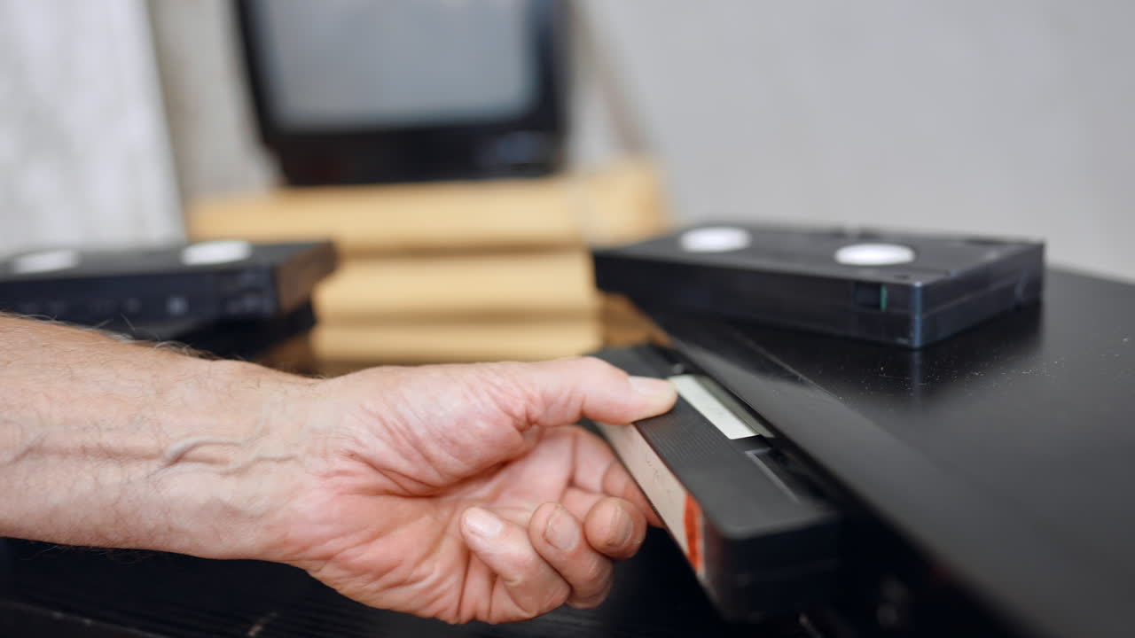 VHS cassette pops out of the player. Male hand takes a cassette from the device. Blurred backdrop