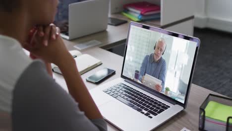 sección media de una mujer afroamericana haciendo una videollamada en una computadora portátil con un colega masculino en la oficina