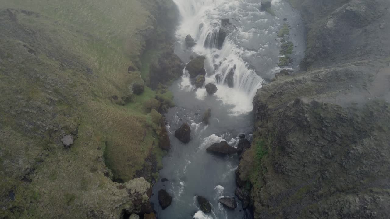 disparo aéreo de un drone de un hermoso río y una cascada en islandia en un día oscuro y brumoso frente a los acantilados y rocas verdes y cubiertos de musgo