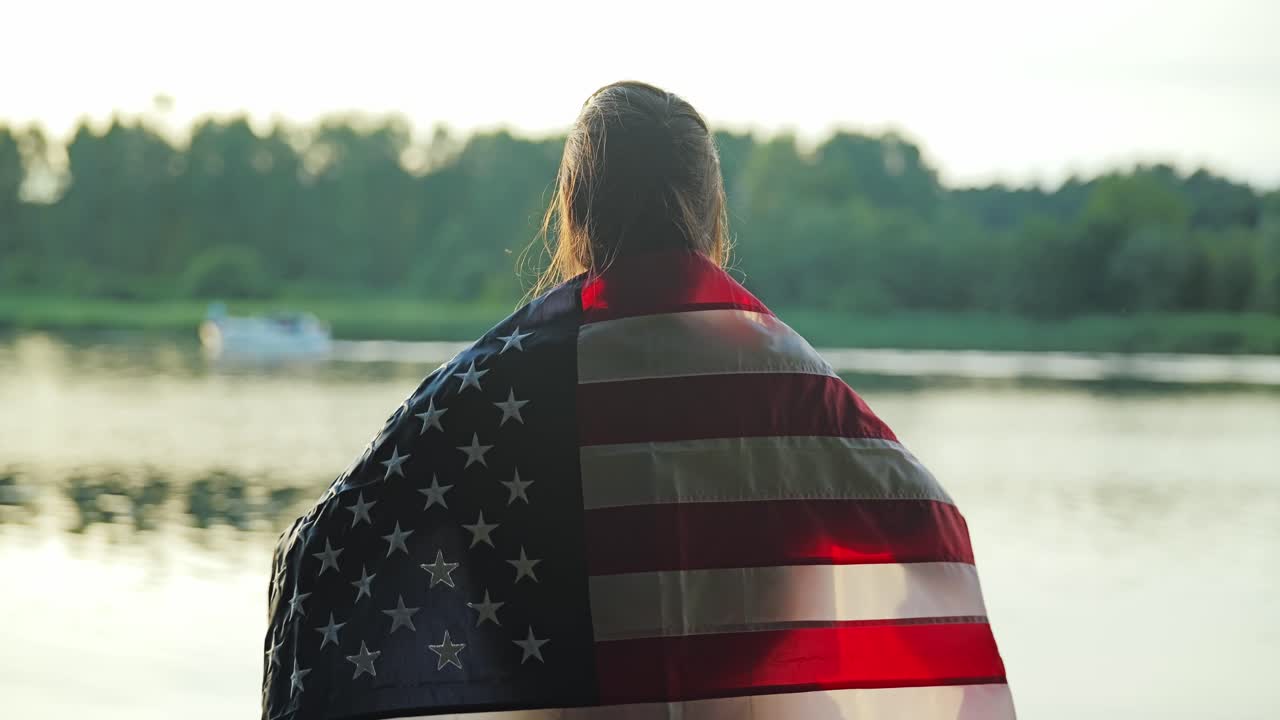 Woman wrapped in US flag extends arms proudly as boat moves behind on river
