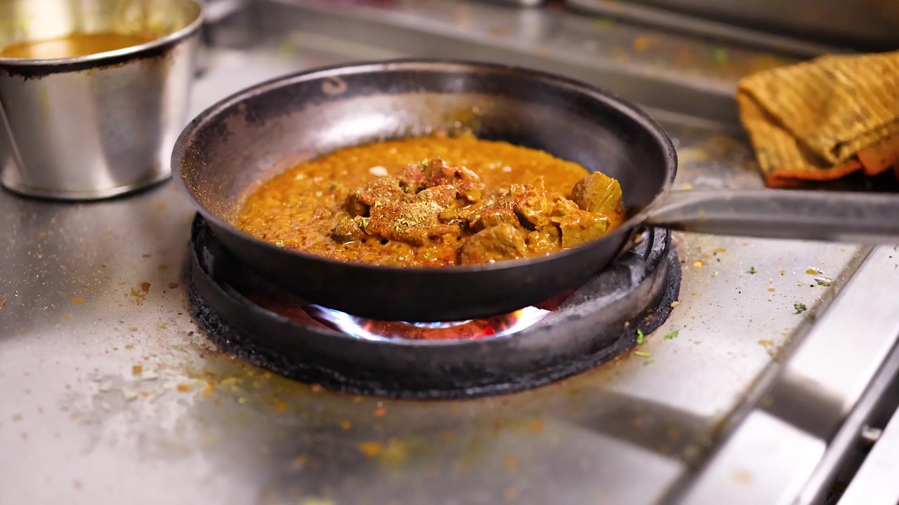 Primo piano di curry indiano che sobbolle in una padella su una fiamma a gas blu