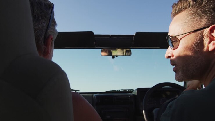 Coppia gay caucasica felice che guida l'auto e parla in una giornata di sole in spiaggia.