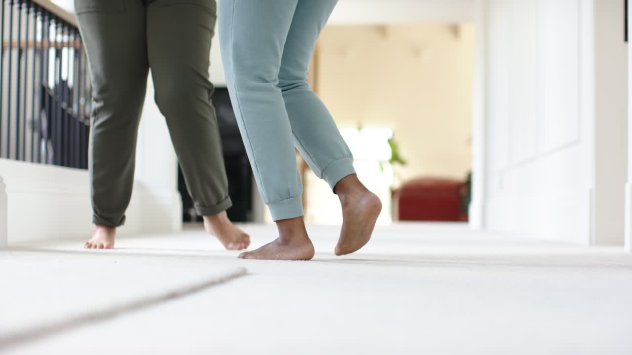 Two barefoot adults are stepping and pivoting on carpeted hallway, open doorway light drawing them