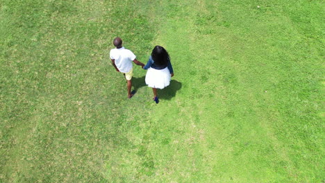 Young-African-American-couple-walking-in-the-open-sunny-grassy-field-while-holding-hands-in-cinematic-4k-30fps
