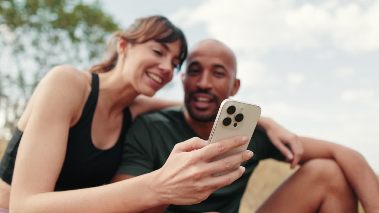 Happy Couple Resting Outdoors and Looking at Smartphone