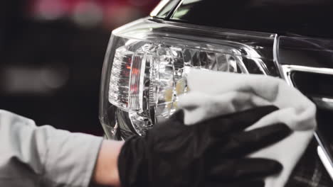 skilled hand in black glove professionally cleans car headlight with precision using a fiber cloth