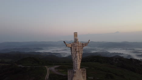 Die-Drohne-Zoomt-Aus-Der-Sicht-Auf-Eine-Hohe-Statue,-Die-Auf-Der-Spitze-Eines-Berges-Steht