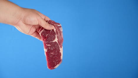 a man's hand holds a steak raw beef ribeye.