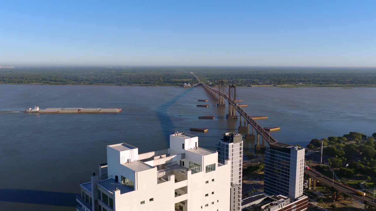 Aerial forward motion over Paraná River showing a cargo ship passing near General Belgrano Bridge and the city of Corrientes, Argentina