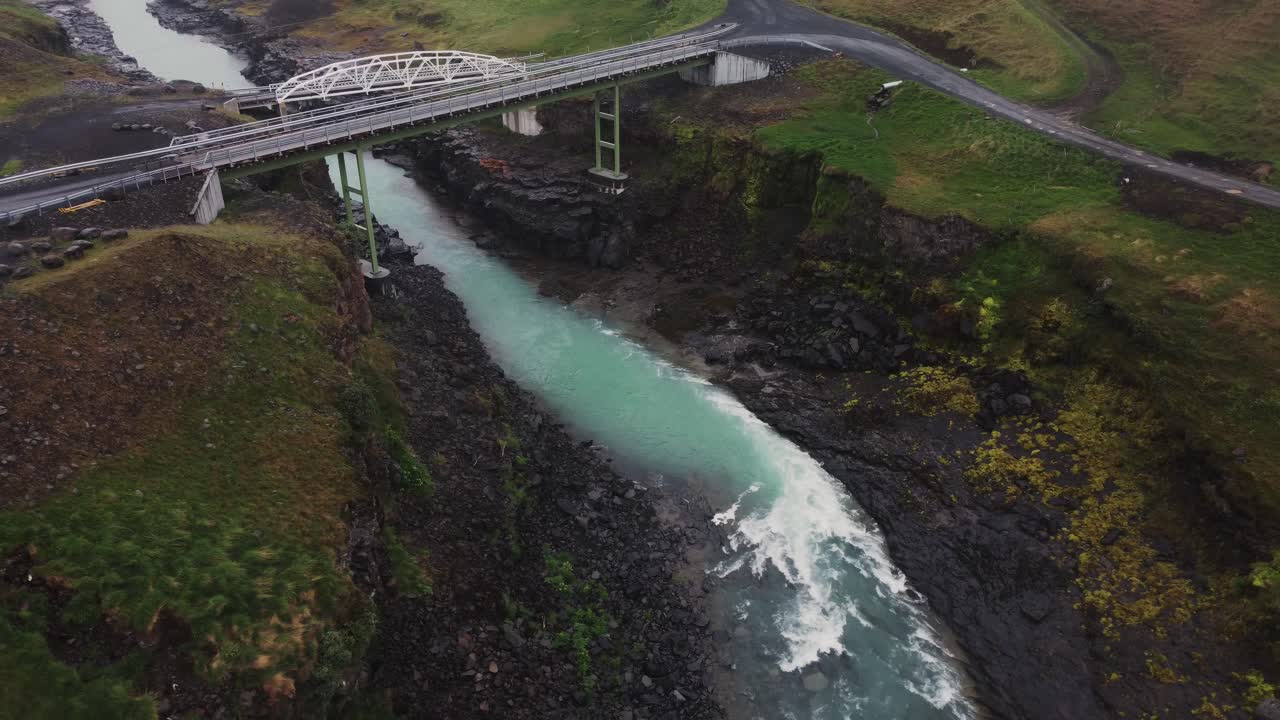 맹렬한 아이슬란드 강과 검은 바위와 급류 위의 다리의 드론  ⁇