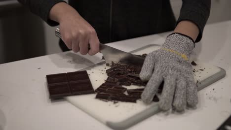 a young girl cuts up dark chocolate before melting it for millionaire shortbread cookies while wearing safety gloves-2