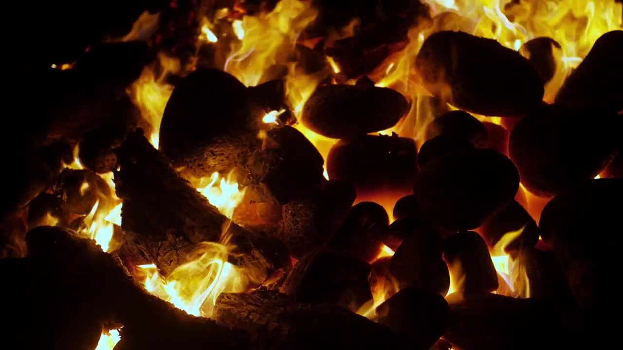 Forno imu hawaiano. Fuoco al rallentatore e pietre roventi in una panoramica molto lenta da sinistra a destra di notte. Cottura tradizionale sotterranea per maiale kalua, laulau e banchetto luau alle Hawaii. Video cinematografico in 4K.