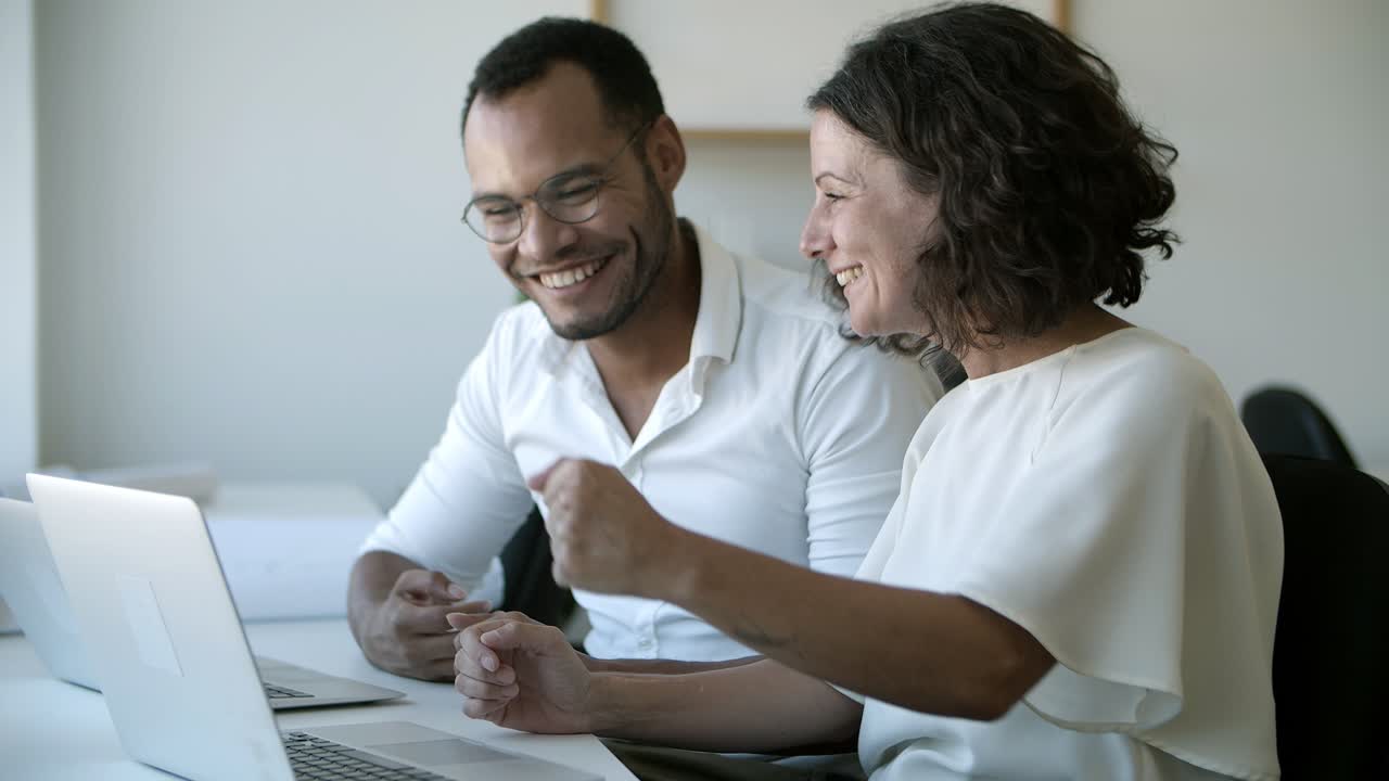 trabajadores sonrientes hablando y apuntando a la computadora portátil