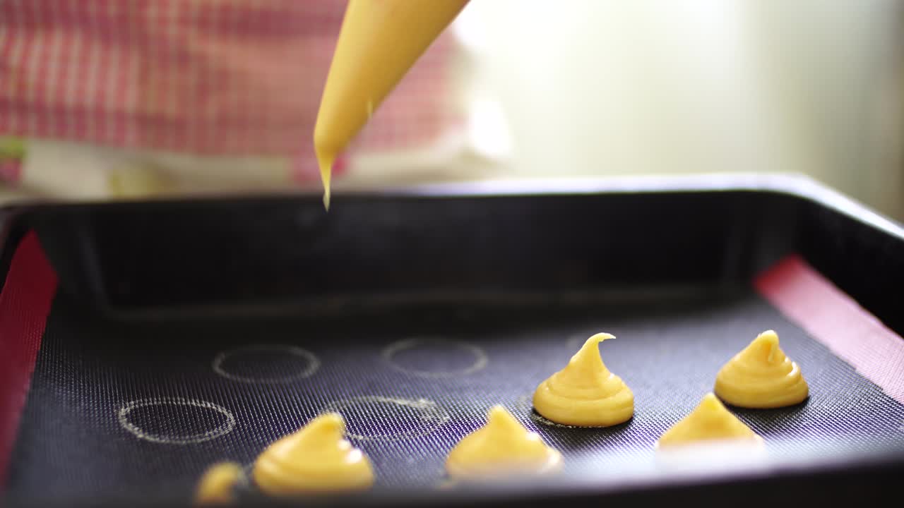 la mano de la mujer exprime la masa del pastel en una sábana de hornear de una bolsa de pastelería