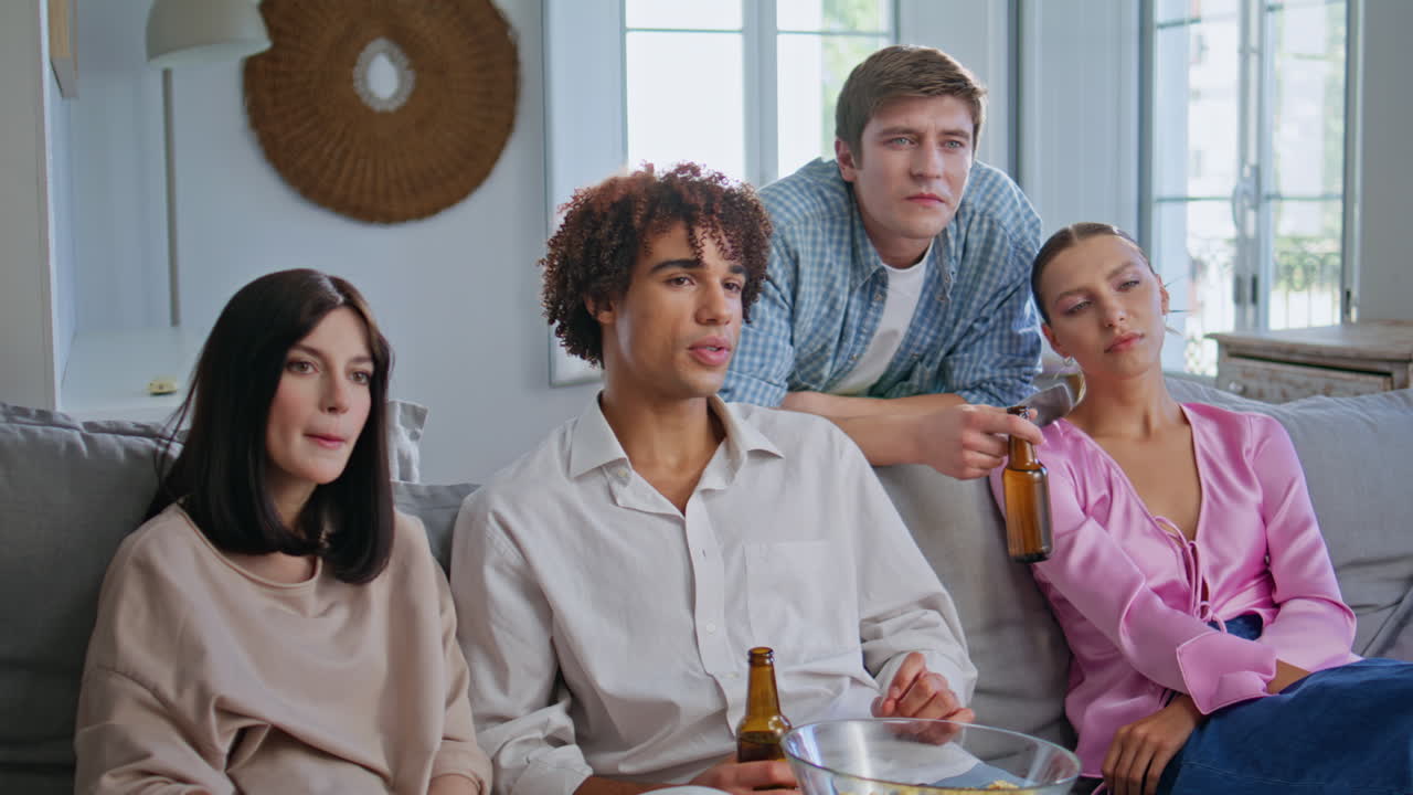 Resting people watching television at light apartment. Friends drinking beer