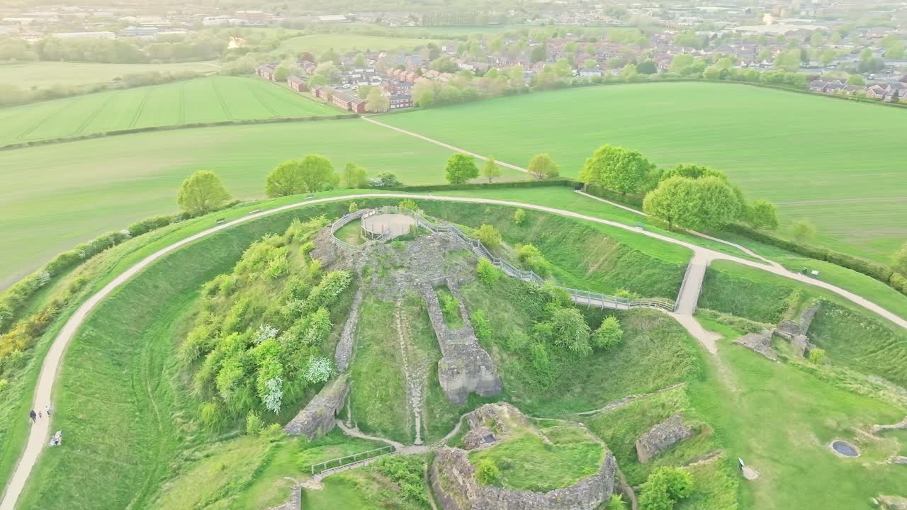 Historic castle ruins stand on high ridge surrounded by open fields and grass, angled orbit, Sandal Castle Wakefield UK