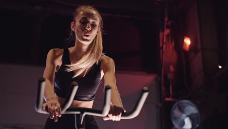 Determined-Young-Woman-Cycling-On-Stationary-Bike-At-Fitness-Studio-1