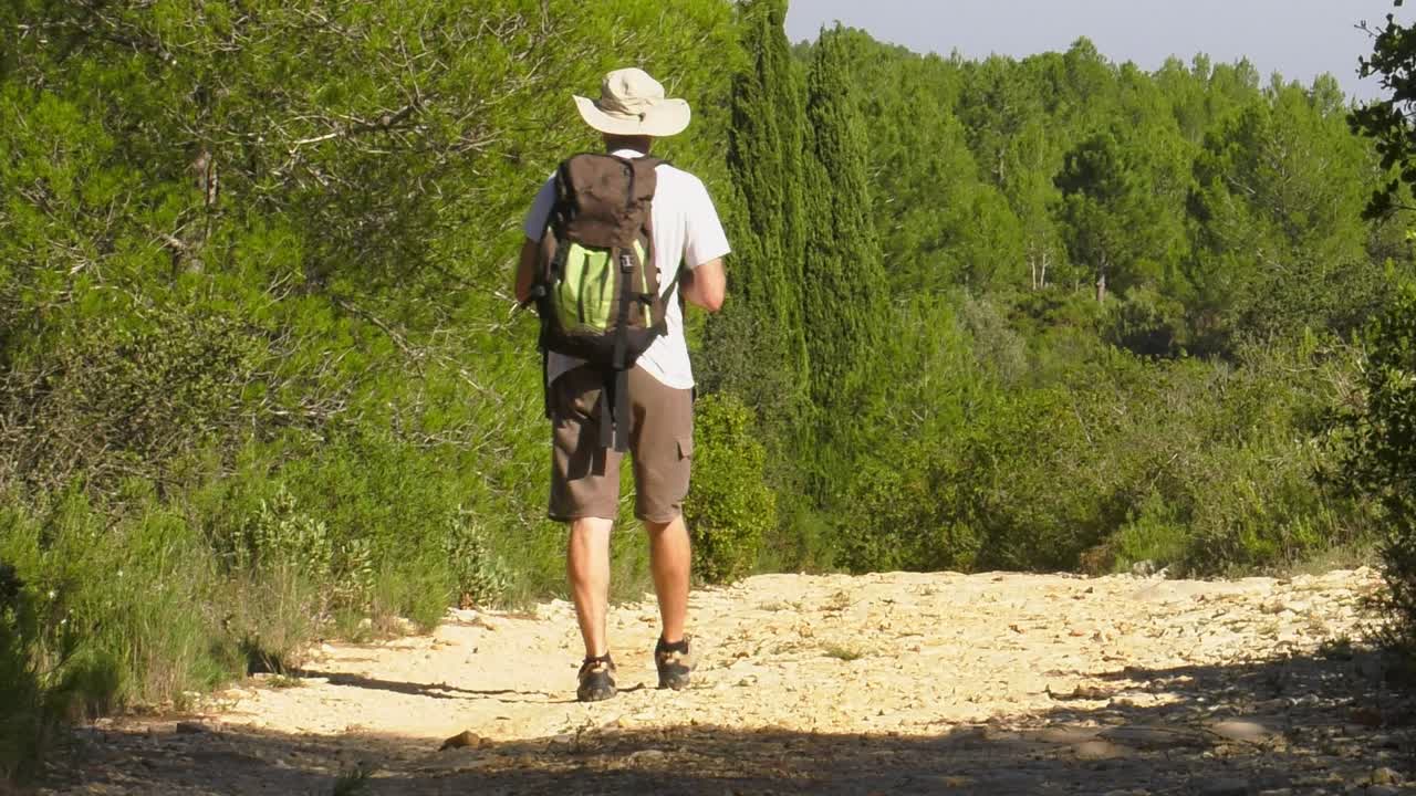 Man on hiking trail with backpack stops to take photo, slow motion