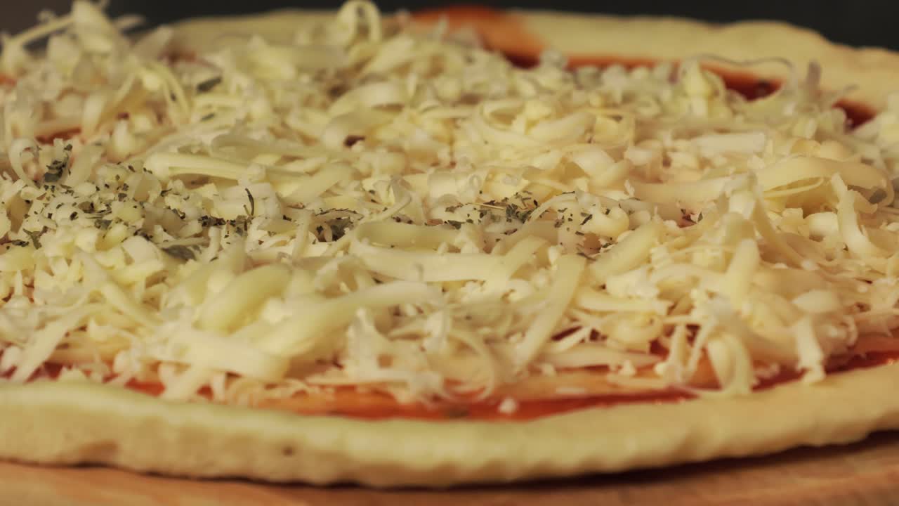 Grated cheese and oregano sprinkled on a pizza dough with tomato sauce, capturing the preparation of a delicious homemade pizza