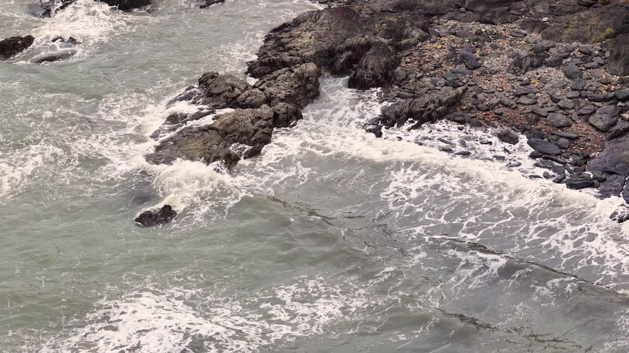 Drone footage captures waves crashing against a rocky shoreline in Port Douglas. Overcast lighting enhances the dramatic ocean scene