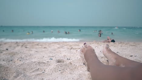 close-feet-of-woman-sunbathing-against-swimming-people