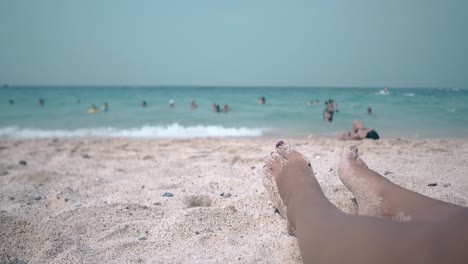 close feet of woman sunbathing against swimming people