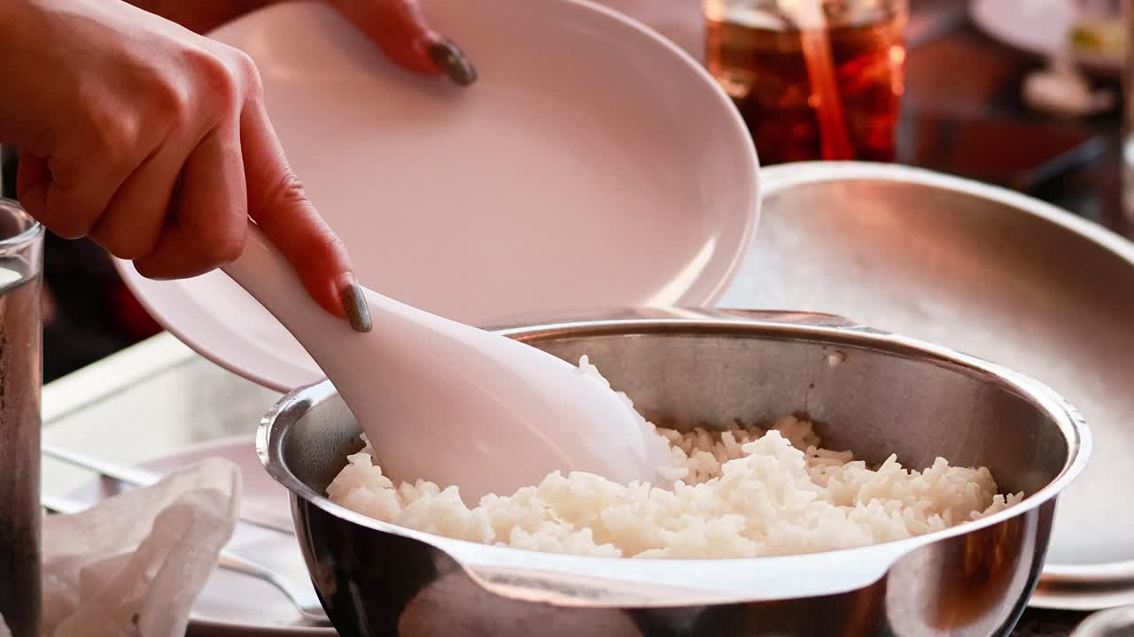 Hands serving rice from pot to plate