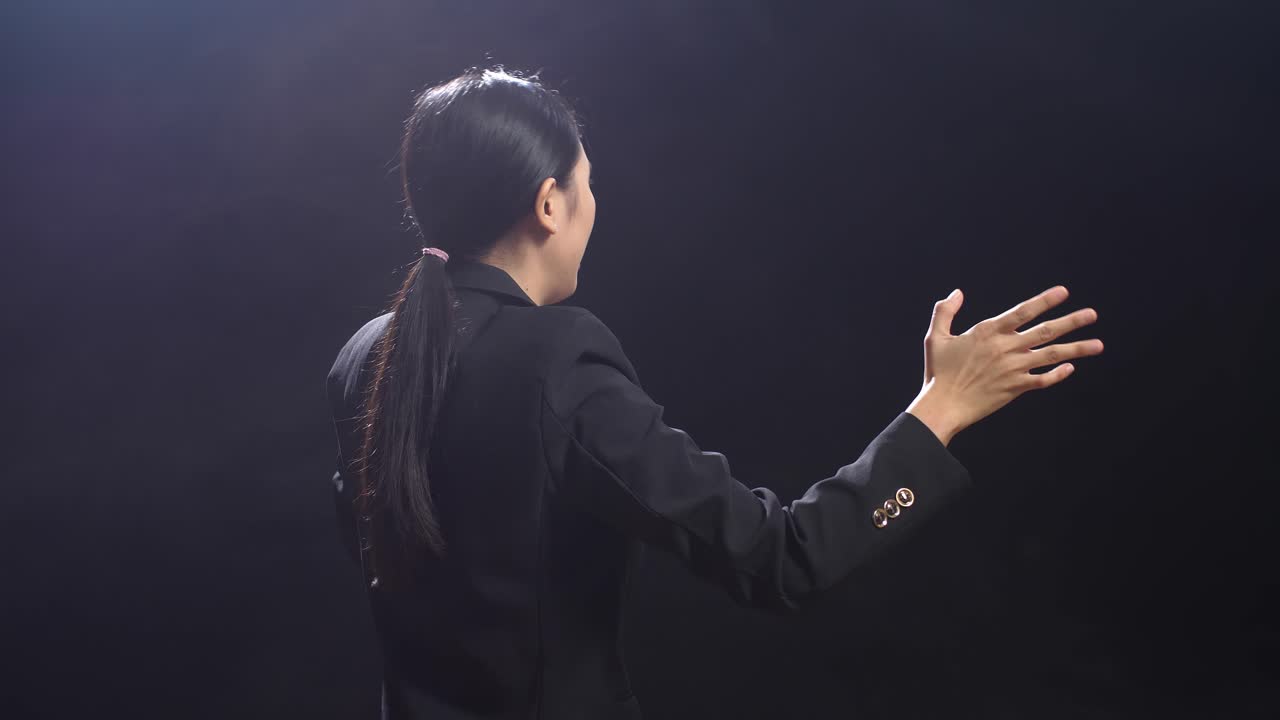 블랙 스크린 스튜디오 에서 연설 하는 동안 손 을 고 있는 비즈니스 슈트 를 입은 아시아어 연설자 의 뒷면