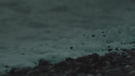 macro view of white wash from foamy ocean wave crashing and dispersing into dark grey pebble beach