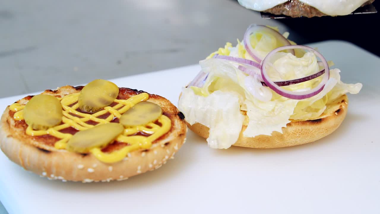 Making fast food. Halves of grilled buns with tasty filling for burger. Cook puts fried meat cutlet with cheese on hamburger. Close-up