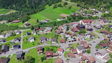 modern houses with solar panels on roof on sunny day in swiss town. green landscape and alps in background. aerial top down shot