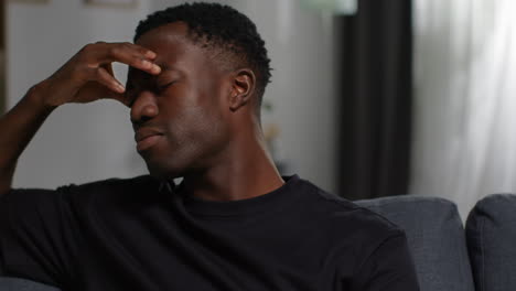 close up of unhappy and depressed young man sitting on sofa at home looking anxious and worried rubbing forehead 3