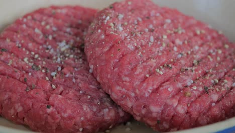 two hamburger patties resting outside while being sprinkled with salt and pepper