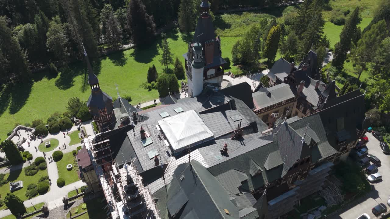 Drone capturing a top-down view of Peleș Castle, highlighting its roofs, towers, and surrounding greenery
