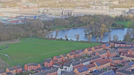 an aerial shot capturing an industrial part of derby, uk being eliminated from private homes area by a string of nature: a green lawn, thick forest, and a still lake