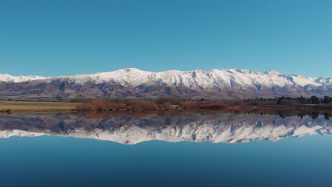 bandada de pájaros blancos volando sobre un lago tranquilo, con un reflejo perfecto de la cordillera y el cielo azul