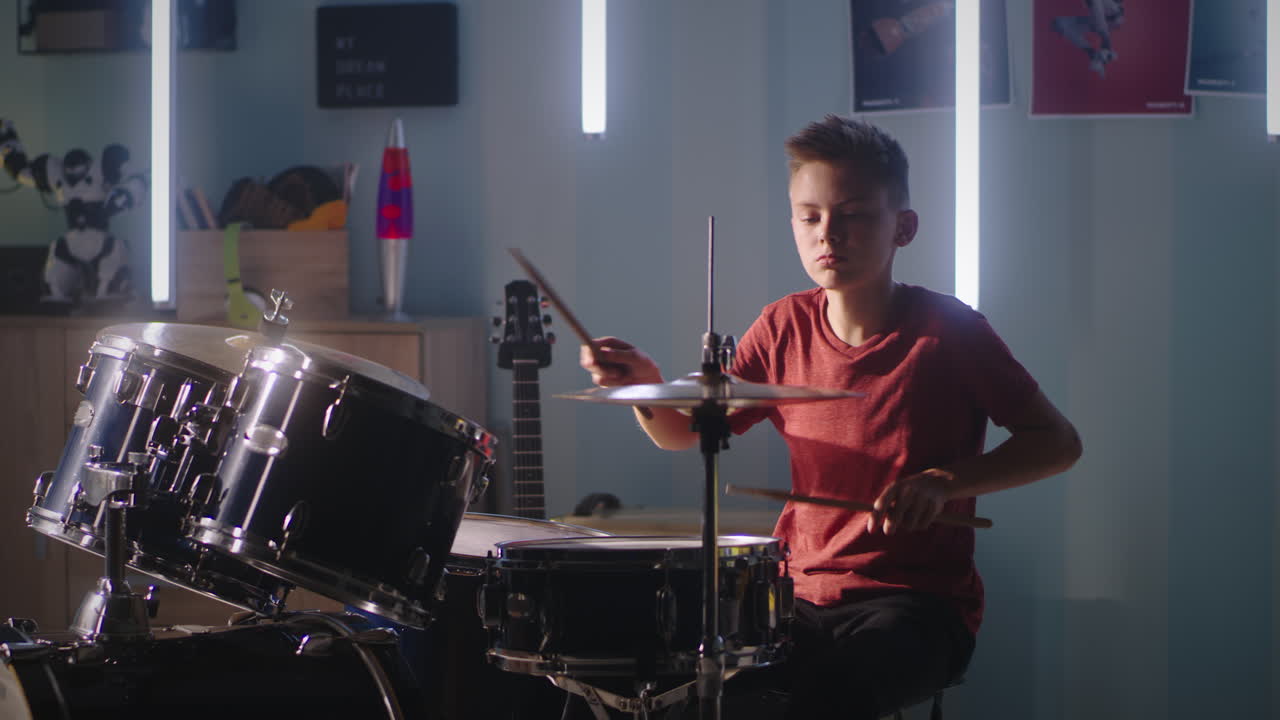 Teen Musician during Rehearsal at Home Teenager in Casual Clothes Learning to Play Drums while Sitting Near Lamps in Illuminated Room during Rehearsal at Home