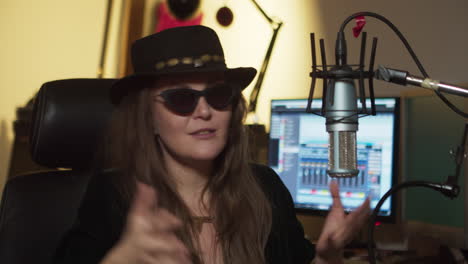 female rocker in black glasses and a hippie hat being interviewed in a recording studio