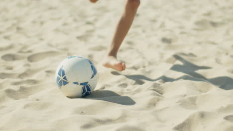 close-up shot of boys feet hitting ball on sandy shore