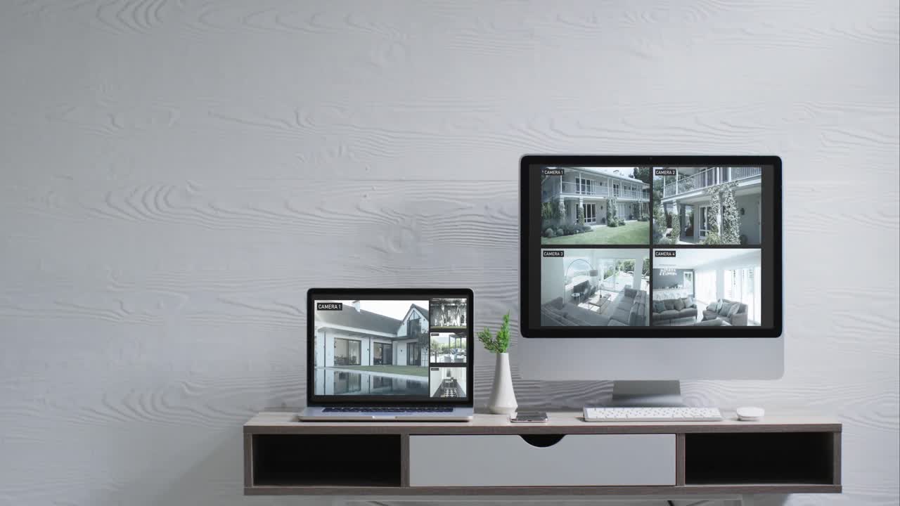 벽에 장착된 컴퓨터 모니터와 책상 위의 노트북과 스크린에 있는 보안 카메라 뷰, 느린 동작