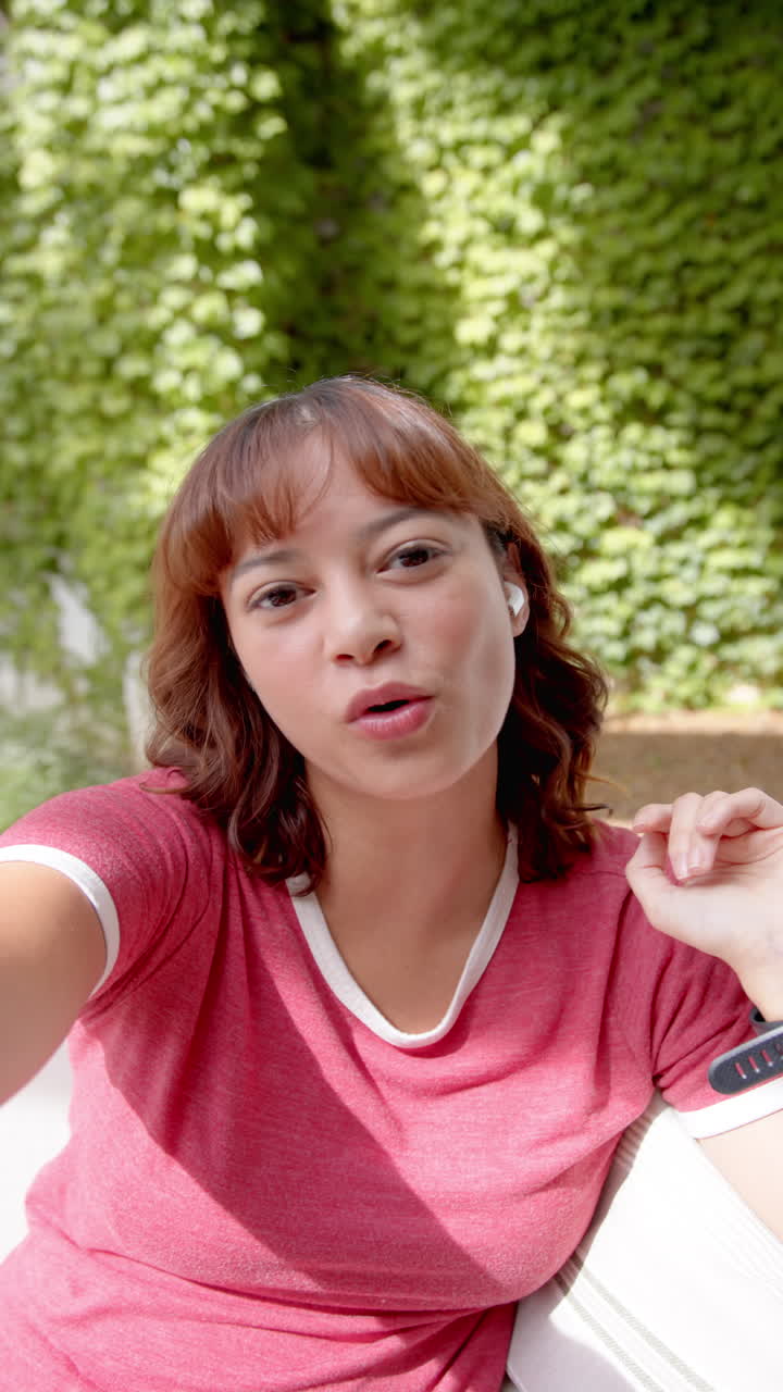 Vertical video: Smiling woman in red shirt taking selfie outdoors, enjoying sunny day