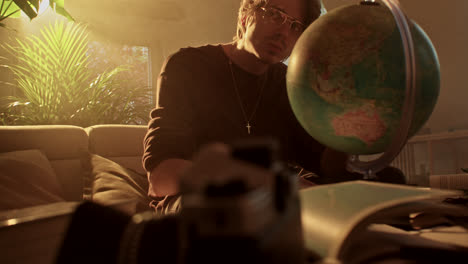 man contemplating a globe in a warm-lit room