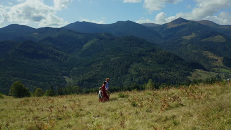 Familia-Caminando-Sobre-Hierba-Divirtiéndose-Juntos-En-La-Vista-Aérea-De-Las-Montañas-De-Verano.