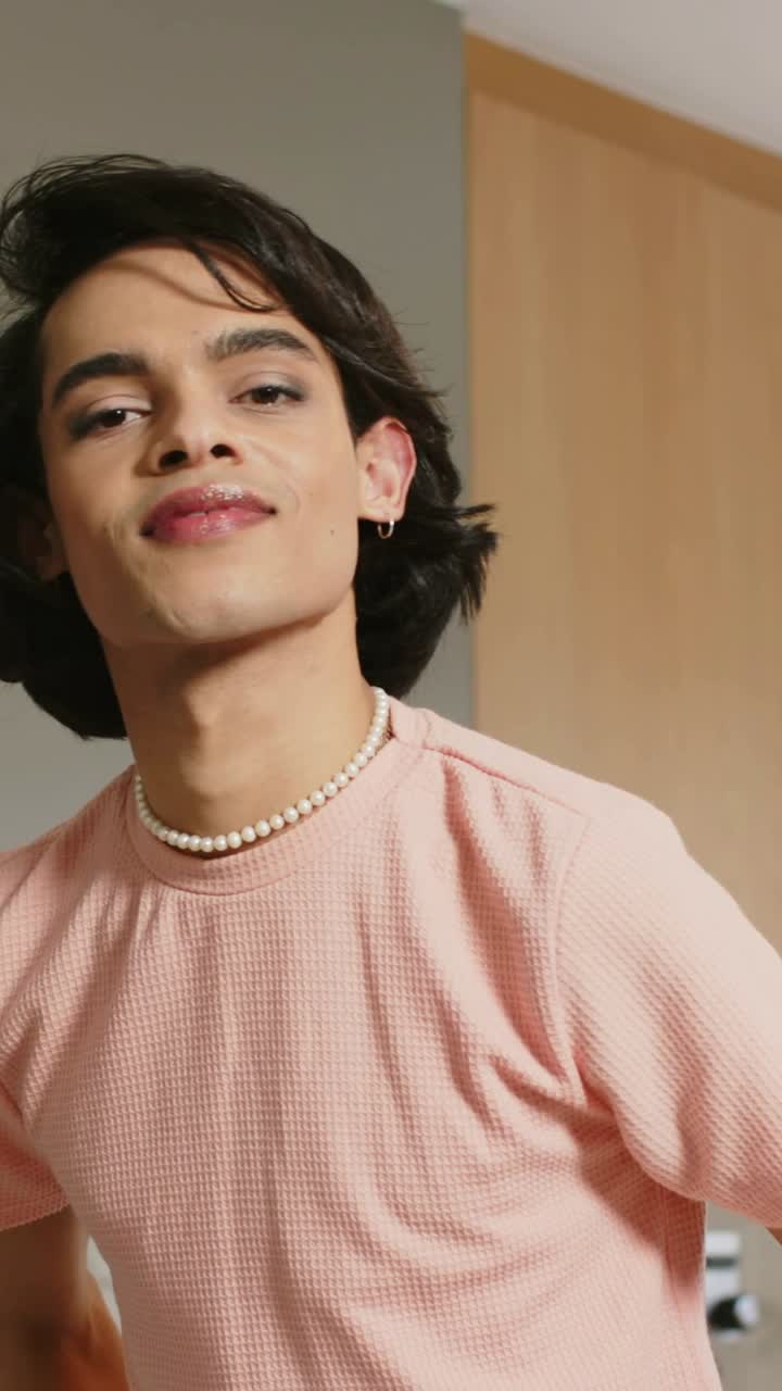 Video verticale: Riprese di un uomo che posa, si inclina e si muove in cucina, con camicia rosa e girocollo di perle.