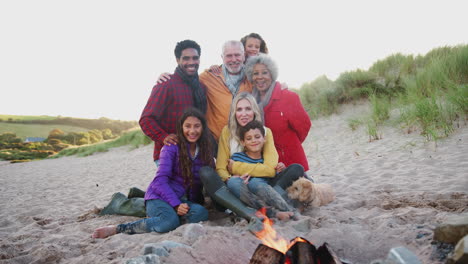 retrato de una familia activa de varias generaciones con un perro mascota sentado junto al fuego en unas vacaciones de playa de invierno