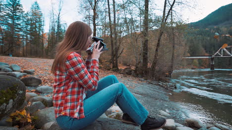 una mujer fotógrafa toma una foto polaroid a lo largo de la orilla del río entre los colores del otoño