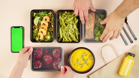 food delivery top view, take away meals in disposable containers. lunch boxes with cooked vegetarian dishes, using phone with chroma green screen. healthy diet. catering service