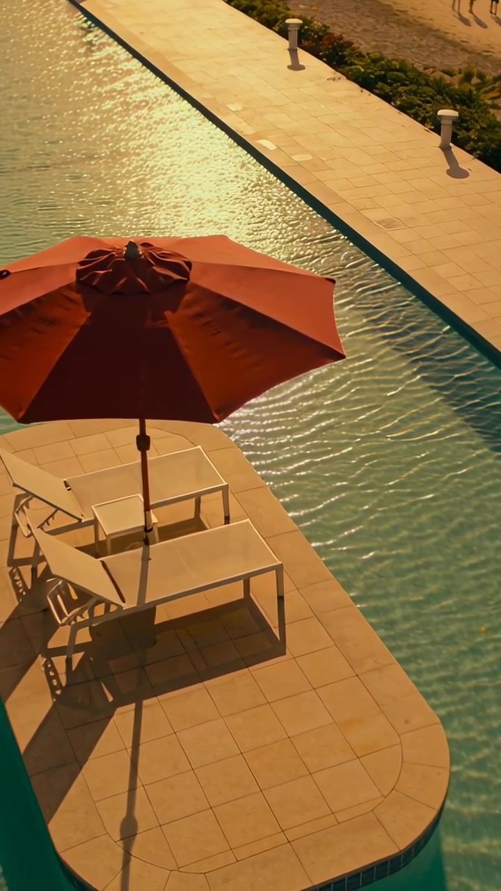 Video verticale: Panoramica che avvicina un ombrellone rosso e sedie bianche a bordo piscina.